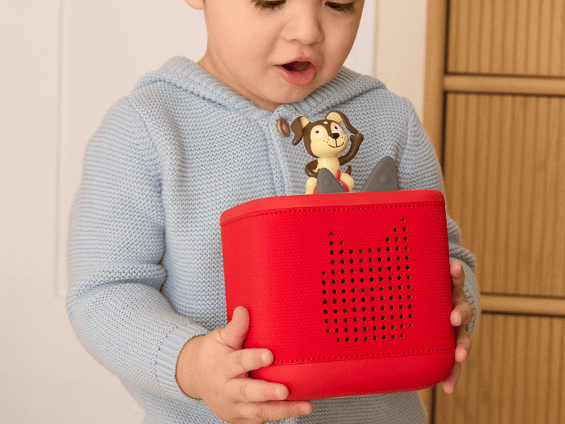 Child holding red TonieBox with monkey Tonie figure on top in home setting