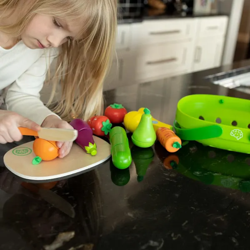 Child playing with toy vegetables and a cutting board on a kitchen counter.
