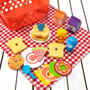 Colorful toy picnic set with pretend food on a red and white checkered tablecloth with a basket in the background.