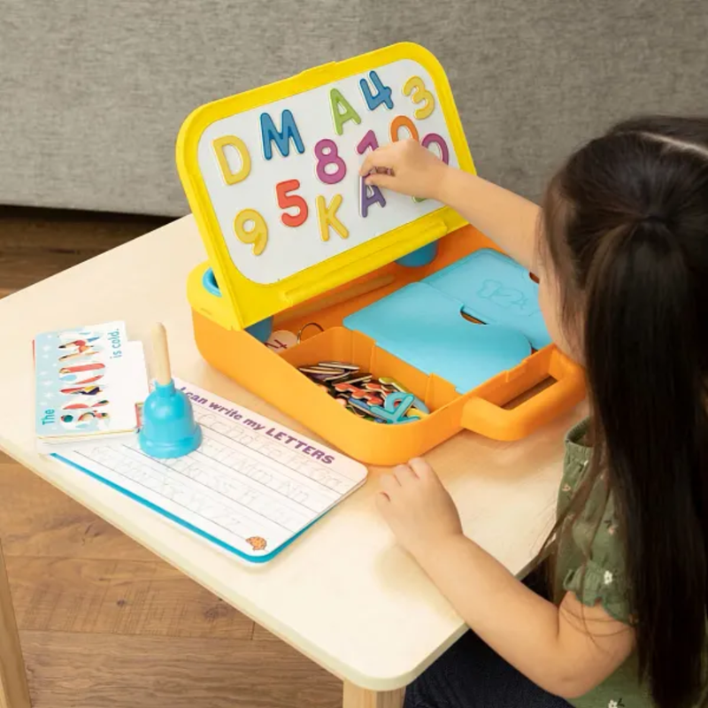 Child using a educational toy with letters and numbers on a table.