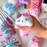 Hand squeezing pink Purrfect Pals cat squishy plush on colorful desk setup.