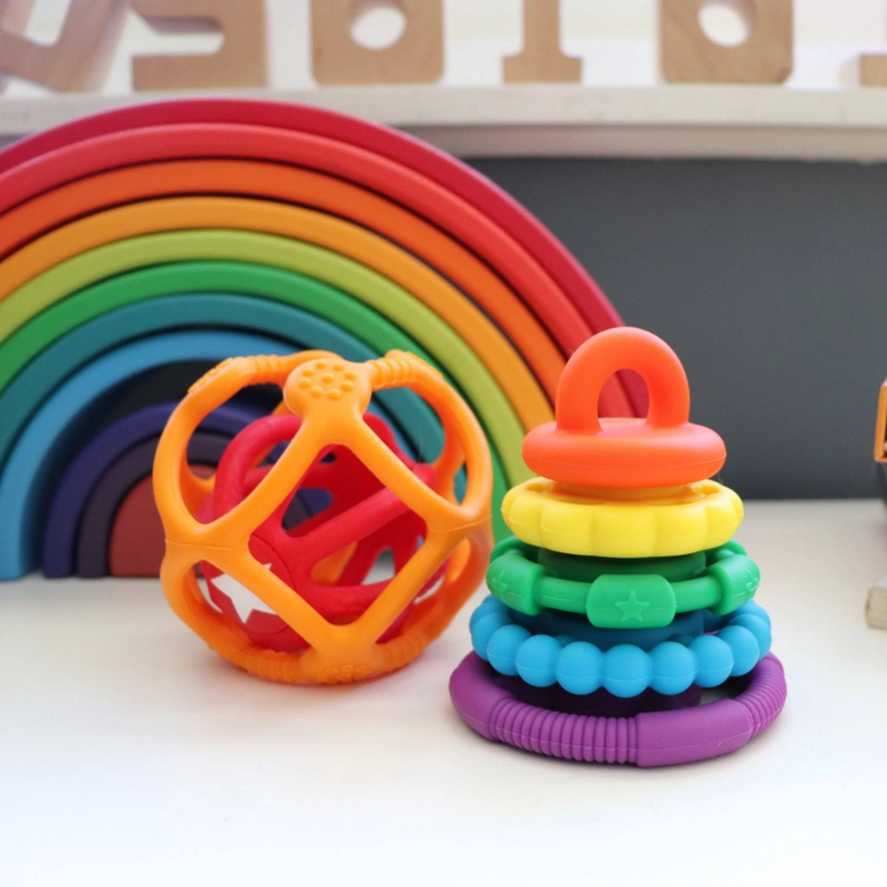 Colorful baby toys including a rainbow stacker, geometric ball, and ring set on a white surface.