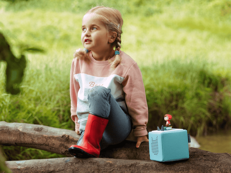 Child sitting outdoors with blue Toniebox and Tonie figure playing fairy tales