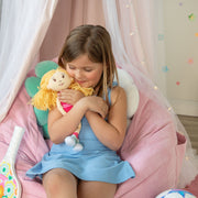 Young girl hugging a Groovy Girls plush doll with yarn hair inside a pink canopy play area