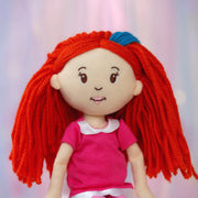 Close-up of Poppy a Groovy Girl plush doll with red hair and a pink shirt on a light background.