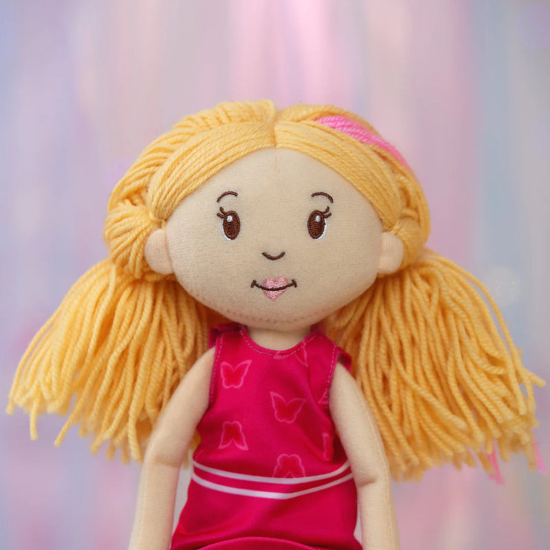 Close-up of Groovy Girls Rose plush doll with blonde hair and a pink dress against a blurred background.