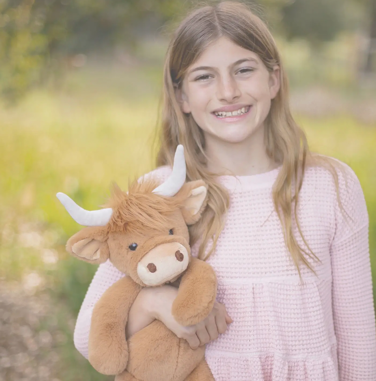 Girl holding brown Highland cow plush toy with white horns outdoors