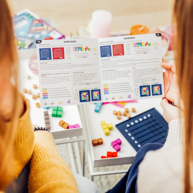Person reading Genius Square game rules with colorful puzzle pieces and game board visible.