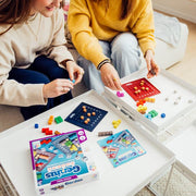 Two people playing Genius Square puzzle game with colorful blocks and dice on table.