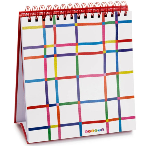 A spiral-bound watercolor pad with a white page featuring a colorful plaid grid pattern, standing on a red base with a red spiral coil.