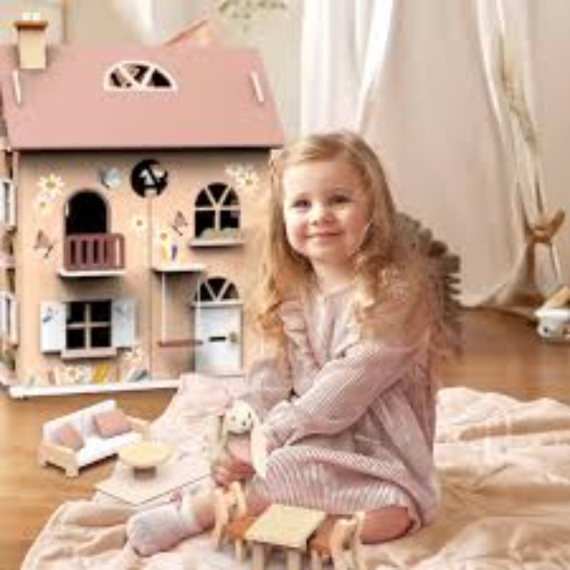 Young girl playing with a wooden dollhouse and toys in a cozy room.