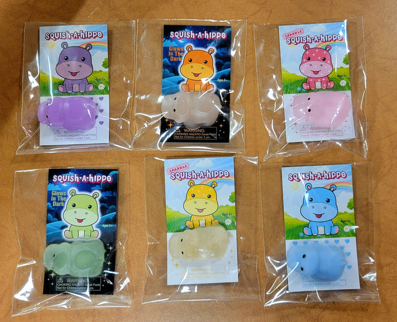 Six packaged Squish-A-Hippo stress toys in different colors including glow-in-dark and sparkle variants