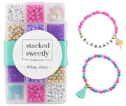 A DIY bracelet kit in a clear plastic organizer box with a turquoise ribbon, shown alongside two finished beaded bracelets: one with black letter beads spelling CELEBRATE and one with a turquoise tassel charm. The kit contains pink, purple, teal, gold, and white beads.