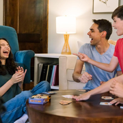 People laughing and playing a card game together in a cozy living room.