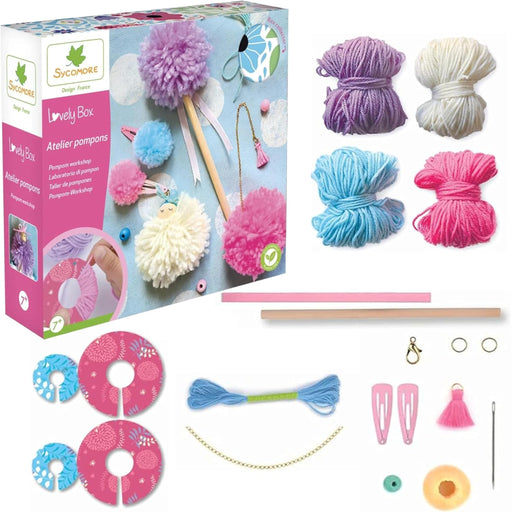 Sycordure Lovely Box pom-pom craft kit shown with its retail box and all included materials laid out on a white background. The kit contains multiple balls of yarn in purple, cream, light blue, and pink, wooden sticks, patterned donut-shaped discs, blue and pink thread, clips, a tassel, rings, and other small crafting accessories.