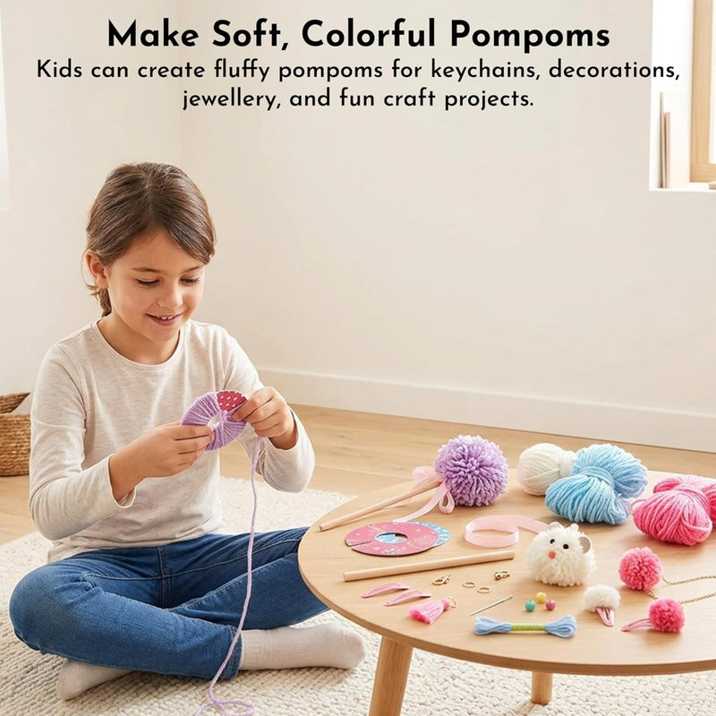 A young girl sits cross-legged on a cream rug, smiling while making a purple pom-pom with yarn. A small round wooden table to her right holds colorful craft supplies including pink, blue, purple, white, and yellow yarn, pom-poms, scissors, and a small plush toy.