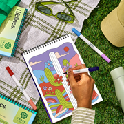 Hand coloring desert cactus scene in trace-by-groove coloring book with colorful markers outdoors