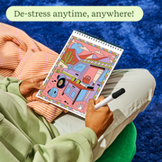 Person coloring desert-themed trace-by-groove art pad with stylus in relaxed setting