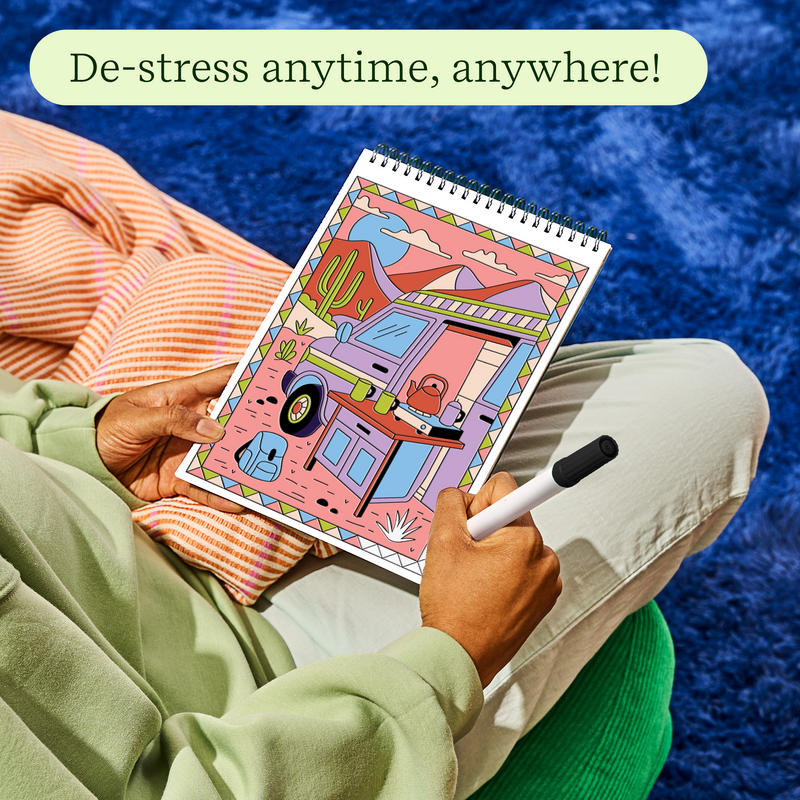 Person coloring desert-themed trace-by-groove art pad with stylus in relaxed setting