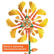 A colorful mechanical flower wind spinner with yellow petals, orange and green accents, and a central gear system, shown on a white background with an orange text banner at the bottom left that reads 'Build a spinning mechanical flower'.