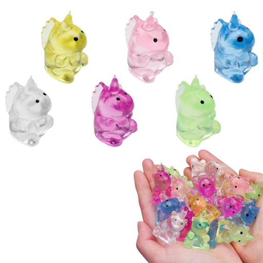 Six small translucent unicorn squishies in different colors are shown on a white background, with a pair of hands holding a handful of more colorful unicorn charms in the lower right corner.