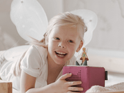 Child with fairy wings playing with pink Tonie audio player featuring TinkerBell figure