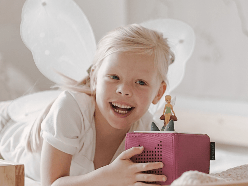 Child with fairy wings playing with pink Tonie audio player featuring TinkerBell figure