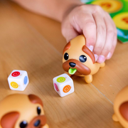 Child's hand interacting with a dog-shaped toy from Tongues Out and dice on a wooden surface.