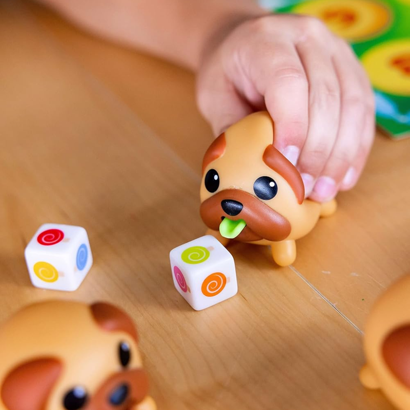Child's hand interacting with a dog-shaped toy from Tongues Out and dice on a wooden surface.