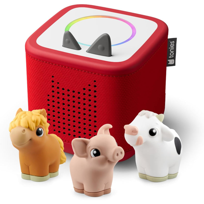 A red Tonies box and with three small farm animal figures in front: an orange horse, a pink pig, and a white cow. The top of the feeder shows a white panel with two gray sensor shapes and a rainbow control ring.
