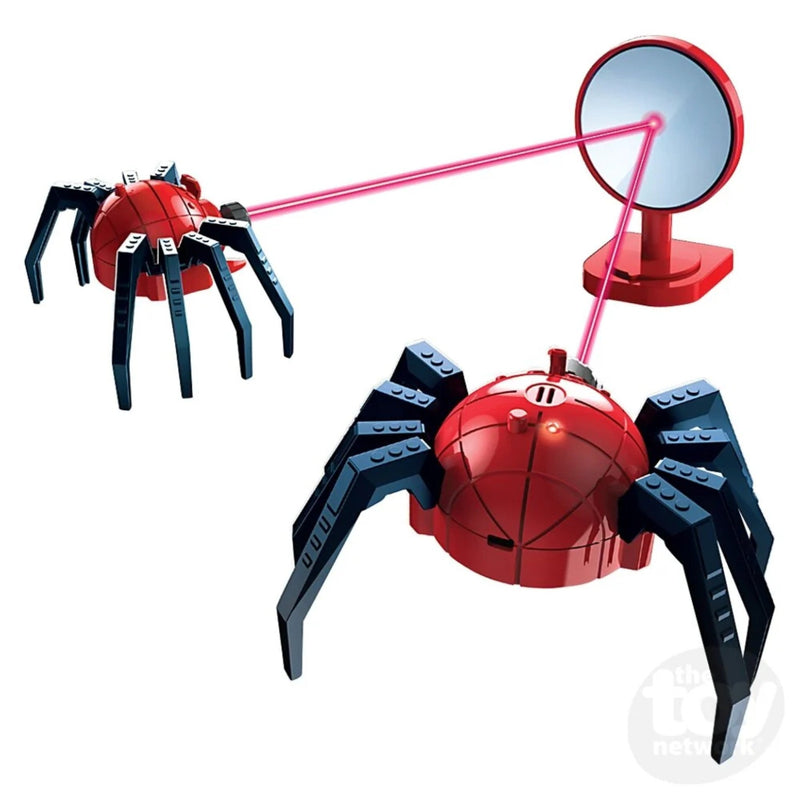 A red and black toy spider robot with a dome-shaped head and eight articulated legs, shown alongside a small red stand with a circular mirror that reflects a pink laser beam toward the spider. The background is solid white.