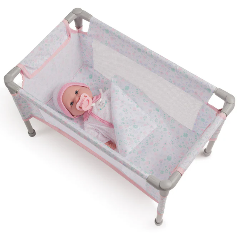 Baby doll in a portable crib with pink and white design on a white background.