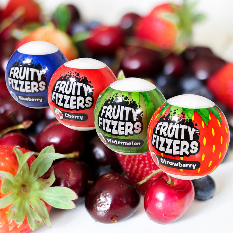 Fruit background with four fruit scented bath bombs:  blueberry, cherry, watermelon and strawberry.