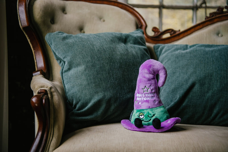 Purple witch hat plushie with green band sitting on vintage chair with teal pillows