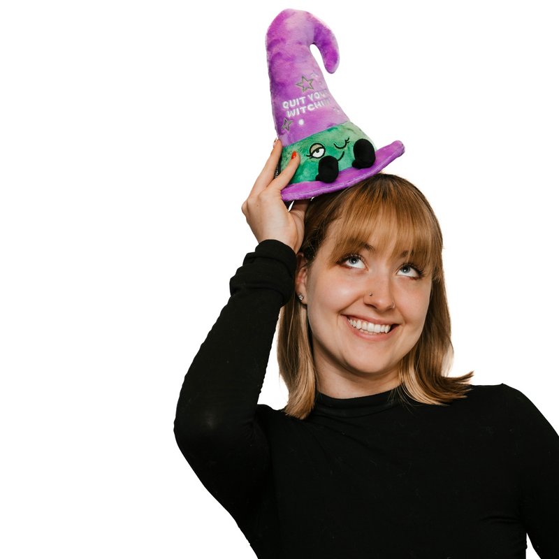 Woman wearing purple witch hat plushie with green face and 'Quit Your Witchin' text