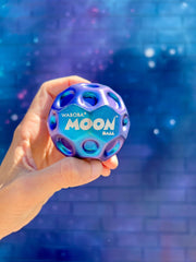 Hand holding blue Waboba Moon Ball against cosmic starry background