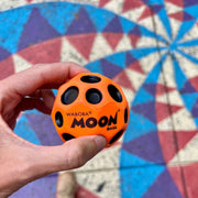 Close up of original Moon Ball orange in color held in a hand on a colorful background.