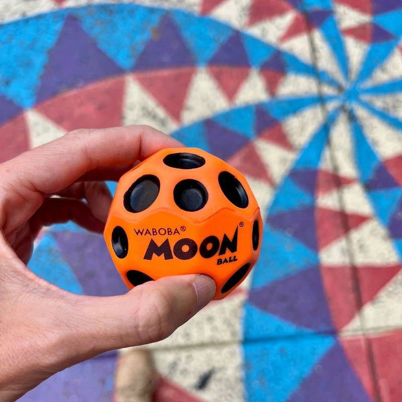 Close up of original Moon Ball orange in color held in a hand on a colorful background.