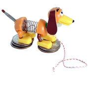 A vintage-style Slinky dog toy made from plastic and metal parts, standing on stacked coins with a red-and-white string attached to its tail, photographed on a plain white background.