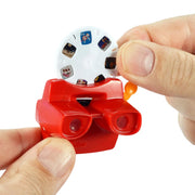 A close-up of a hand using a red World's Smallest Viewmaster toy with a white circular film holder containing printed sample photos, against a plain white background.