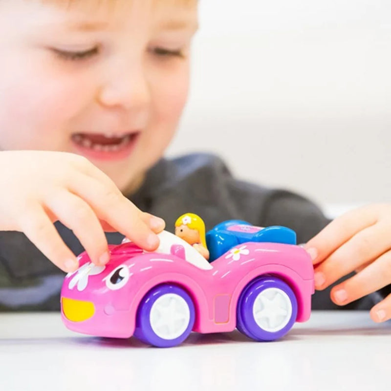 A young child's hands and face are visible as they play with a pink toy convertible car with purple wheels on a white surface.