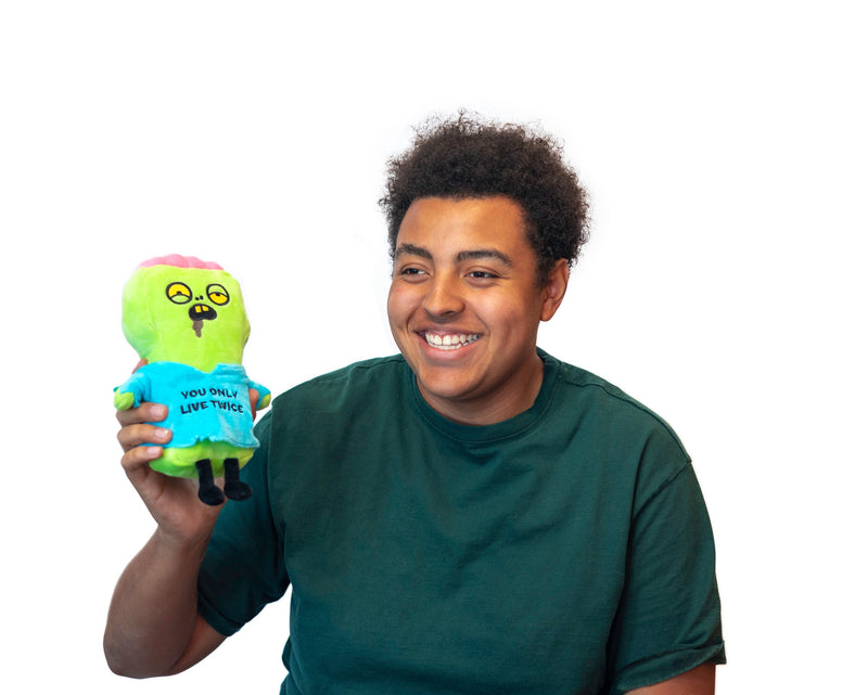 Smiling person holding green zombie plushie with 'You Only Live Twice' text