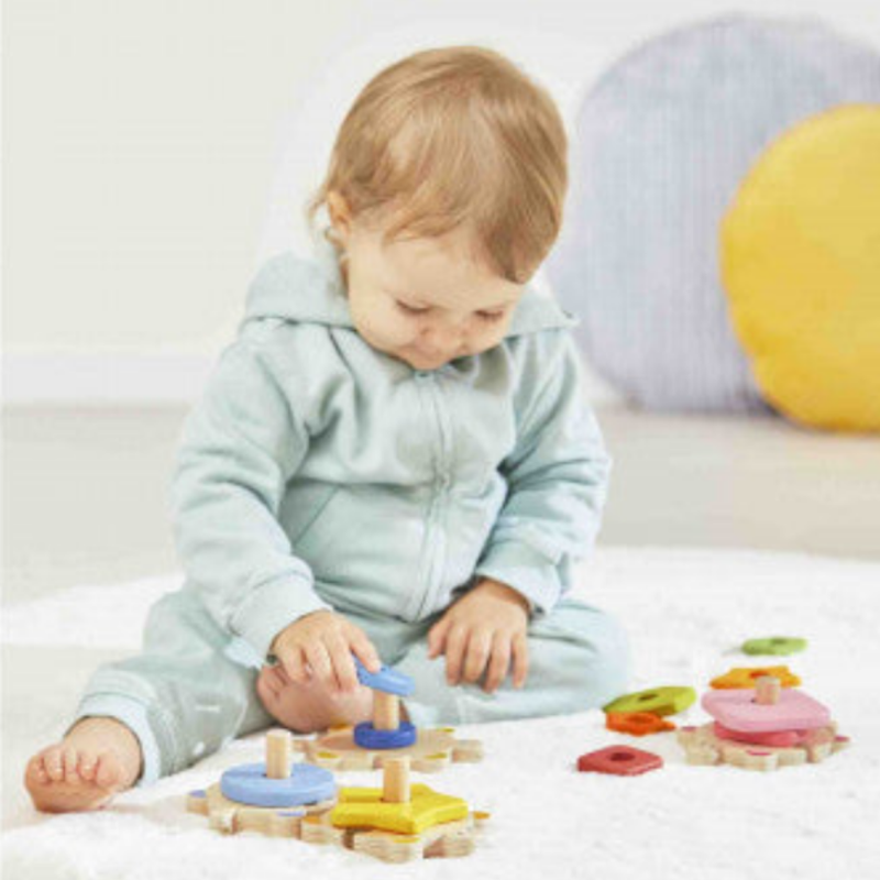 Child playing with colorful Zigolos stackable turtle puzzle toy on white rug.
