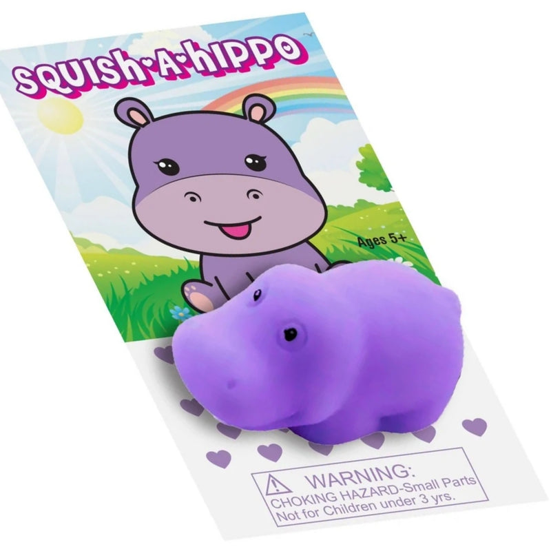 A purple squishy hippo toy partially tucked under its printed retail card packaging. The card features a cartoon hippo, a rainbow, green grass, and a choking hazard warning label at the bottom.