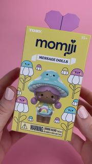 Hand holding Momiji Message Dolls packaging with mushroom character and purple heart backdrop
