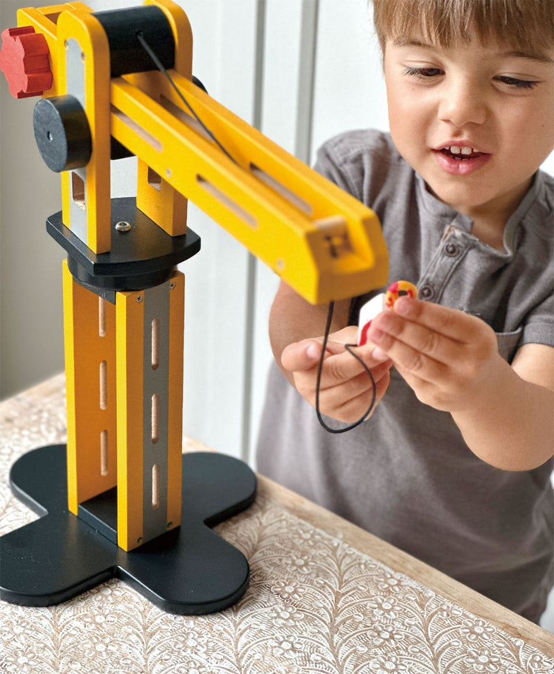 Child playing with yellow wooden crane toy by Mentari