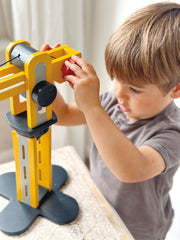Child playing with yellow Mentari wooden crane toy in bright indoor setting