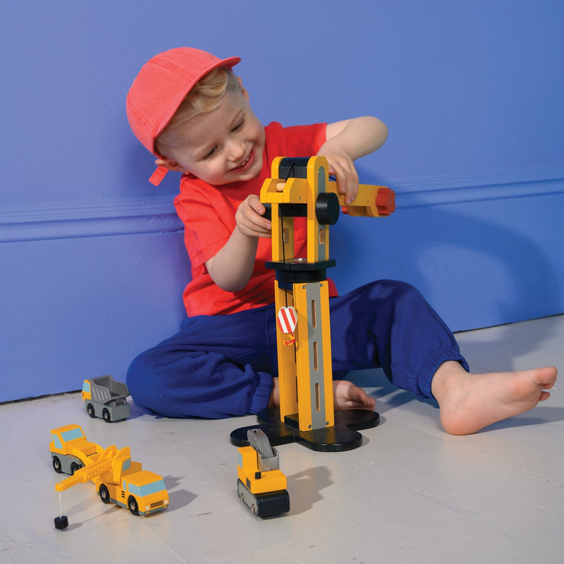 Child playing with yellow Mentari toy crane and construction vehicles in studio setting