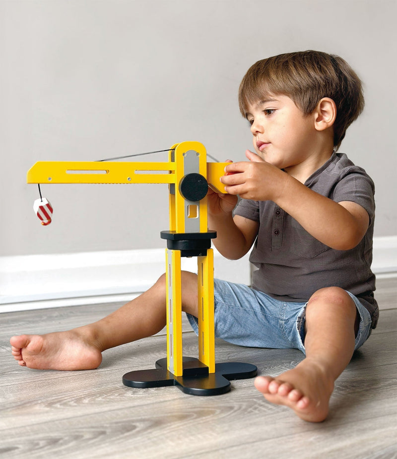 Child playing with yellow wooden toy crane sitting on floor