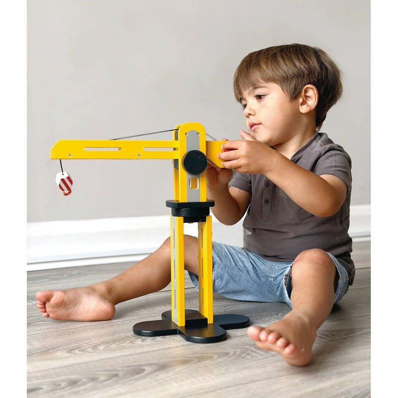 Child playing with yellow wooden toy crane sitting on floor